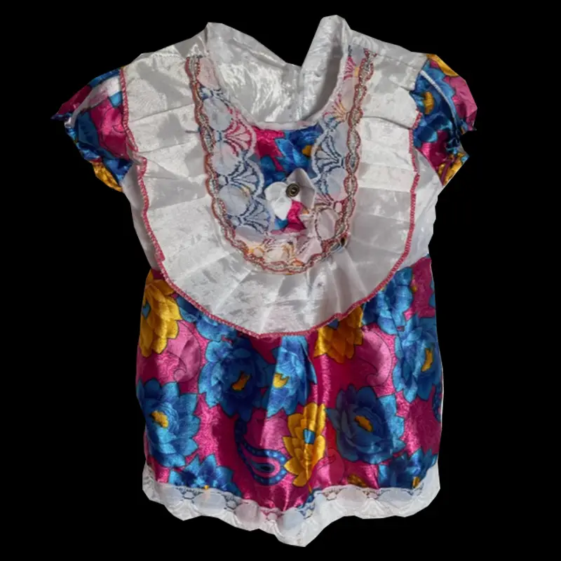 Von Sillas Mutter selbst gen&auml;htes, farbenfrohes Kinderkleid auf schwarzem Hintergrund. Der gl&auml;nzende Stoff zeigt blaue und gelbe Blumen auf pinkem Grund. Das Kleid hat kurze &Auml;rmel, wei&szlig;e Spitze am Saum und einen breiten wei&szlig;en Kragen mit rotem Rand.